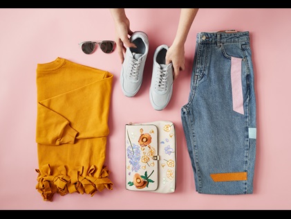 Overhead shot of a woman laying out an outfit including shoes, pants, shirt and accessories. 