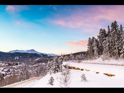 Snow covered and tree-lined Rocky Mountains road with pink and blue sunset skies overhead, Colorado. 