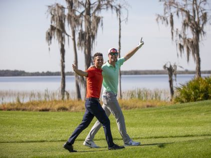 Ben Higgins and Wells Adams waving to the crowd with their arms around their shoulders at the Hilton Grand Vacations Tournament of Champions