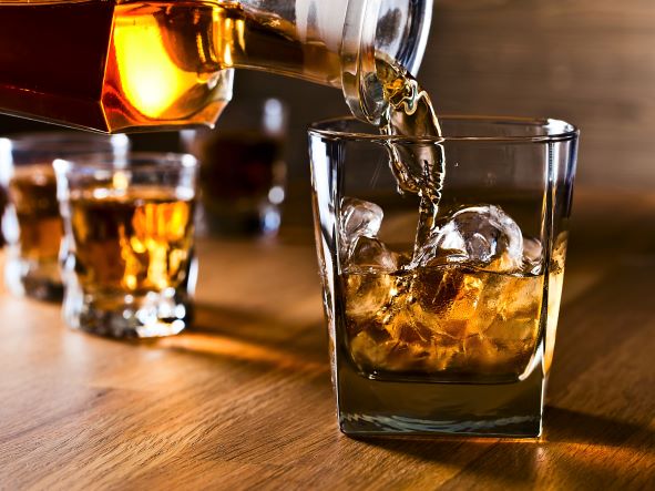 Whiskey pouring into a glass with ice on a wooden table