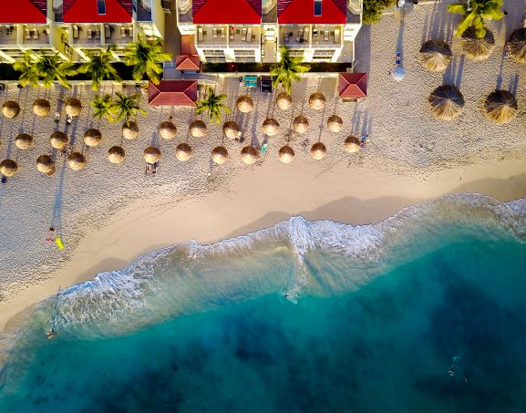Beautiful aerial image of beach umbrellas peppering white sands of a Sint Maarten beach, turquiose waters crashing ashore, Caribbean. 